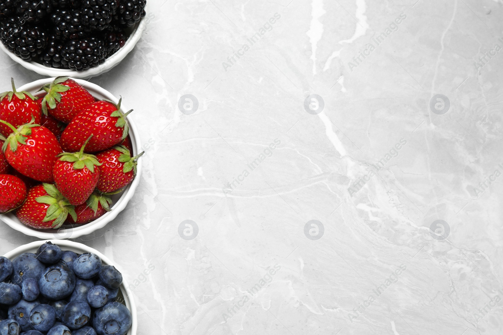 Photo of Different ripe berries on light marble table, flat lay. Space for text