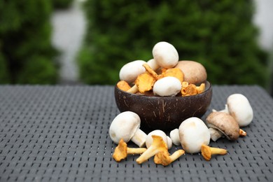 Photo of Bowl with different fresh mushrooms on grey rattan table outdoors. Space for text