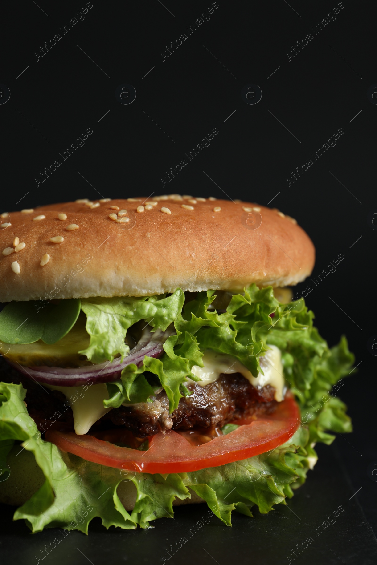 Photo of Delicious burger with beef patty and lettuce on black background, closeup