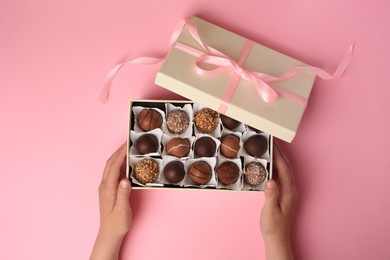 Photo of Child with box of delicious chocolate candies on pink background, top view