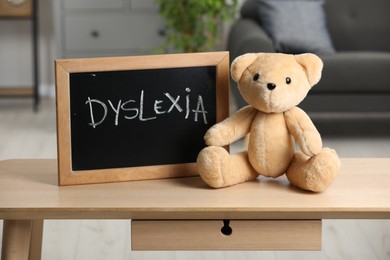 Photo of Teddy bear and small blackboard with word Dyslexia on wooden table in room