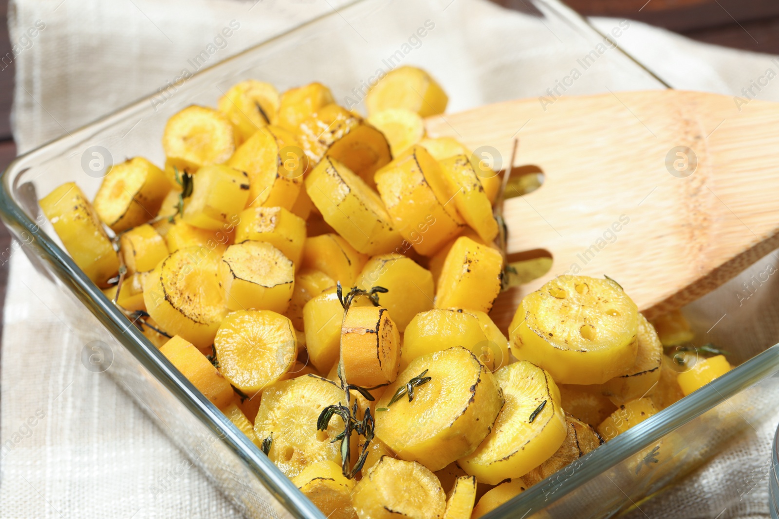 Photo of Baked yellow carrot and wooden fork in glass dish on table, closeup