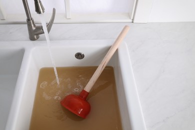 Photo of Clogged kitchen sink with plunger and dirty water