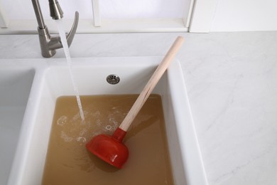 Clogged kitchen sink with plunger and dirty water