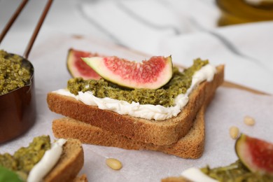 Photo of Tasty bruschetta with cream cheese, pesto sauce and fig on parchment paper