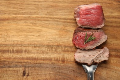 Photo of Delicious sliced beef tenderloin with different degrees of doneness on wooden table, top view. Space for text