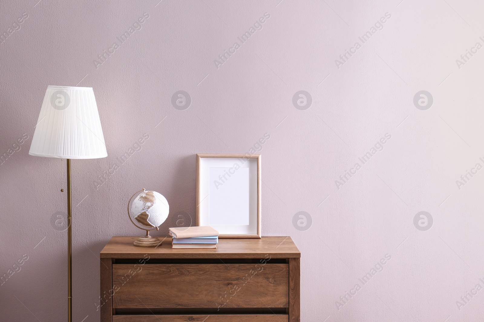 Photo of Wooden chest of drawers with globe, books and empty frame near beige wall in room, space for text. Interior design