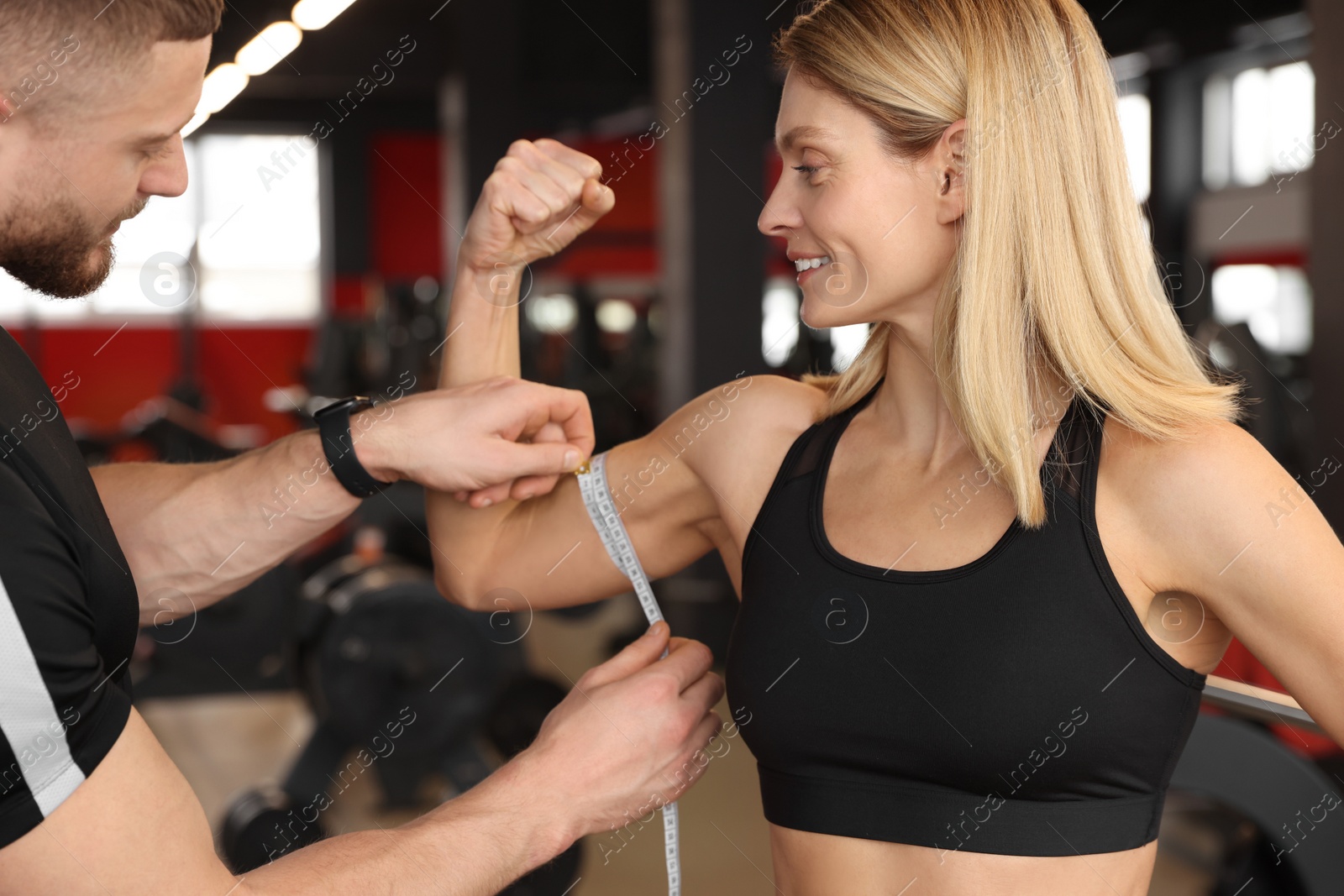 Photo of Trainer measuring woman`s biceps with tape in gym