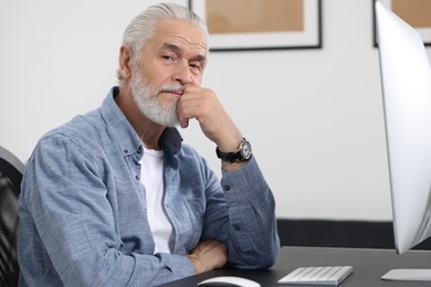 Photo of Handsome senior man working on computer at table in office. Space for text