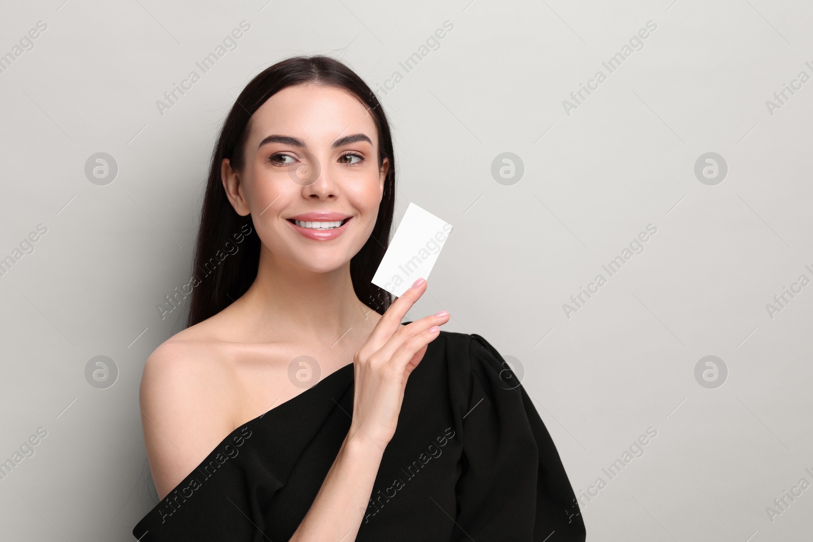 Photo of Happy woman holding blank business card on light grey background. Space for text