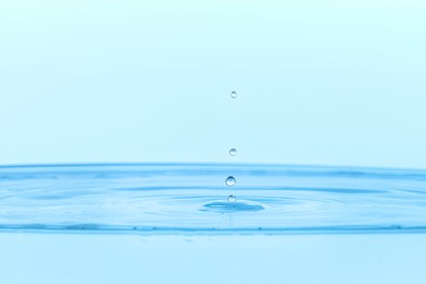 Photo of Drops falling into clear water on light blue background, closeup