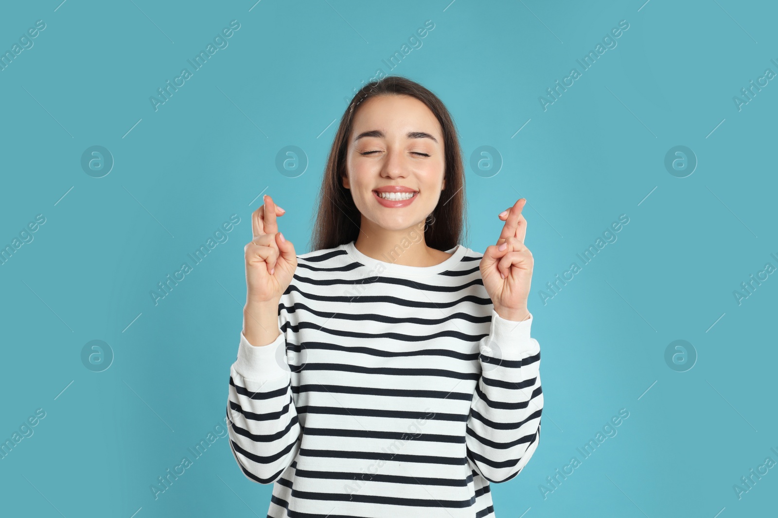 Photo of Woman with crossed fingers on light blue background. Superstition concept