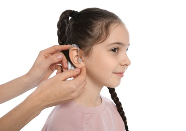 Young woman putting hearing aid in little girl's ear on white background