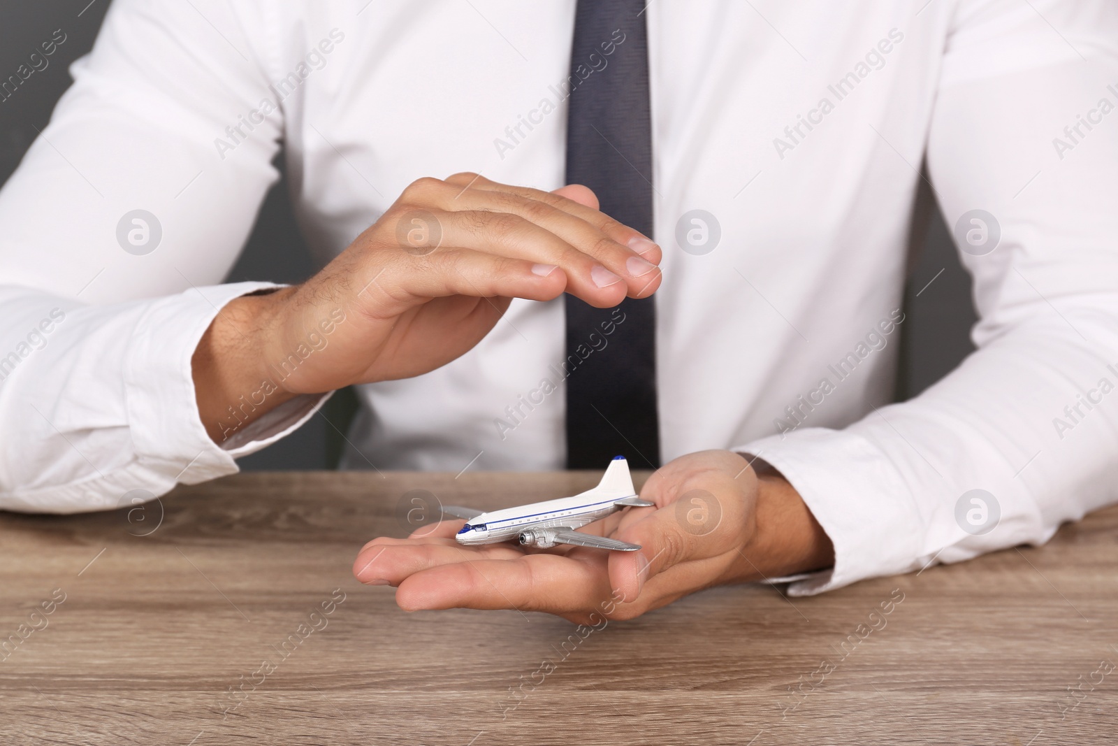 Photo of Insurance agent covering toy plane at table, closeup. Travel safety concept