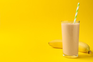 Photo of Glass of tasty banana smoothie with straw and fresh fruit on yellow background. Space for text