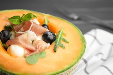 Photo of Half of melon with prosciutto, blueberries and herbs on table, closeup