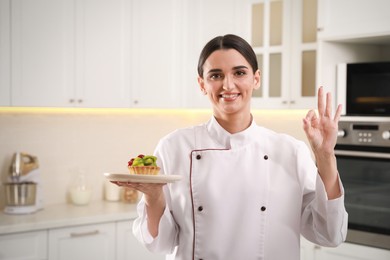 Photo of Happy professional confectioner with tartlet showing okay gesture in kitchen
