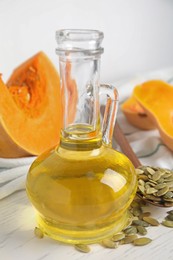 Photo of Glass jug of oil with pumpkin seeds on white wooden table, closeup