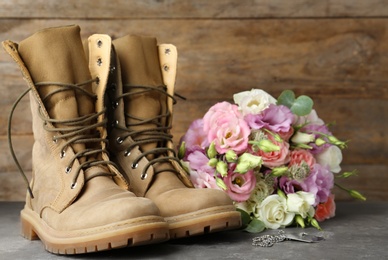 Photo of Military boots with flowers on grey stone surface, space for text. Armed Forces Day