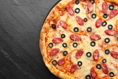 Photo of Tasty pizza with cheese, dry smoked sausages, olives and pepper on grey table, top view. Space for text