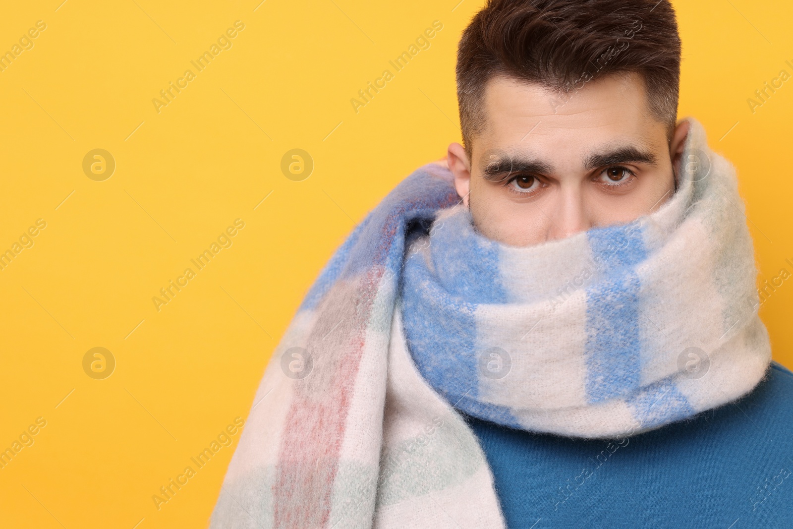Photo of Man hiding in warm scarf on yellow background. Space for text