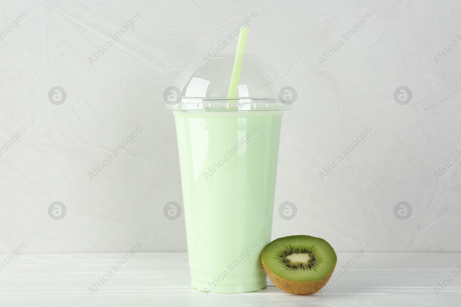 Photo of Plastic cup of tasty smoothie and fresh kiwi on white wooden table