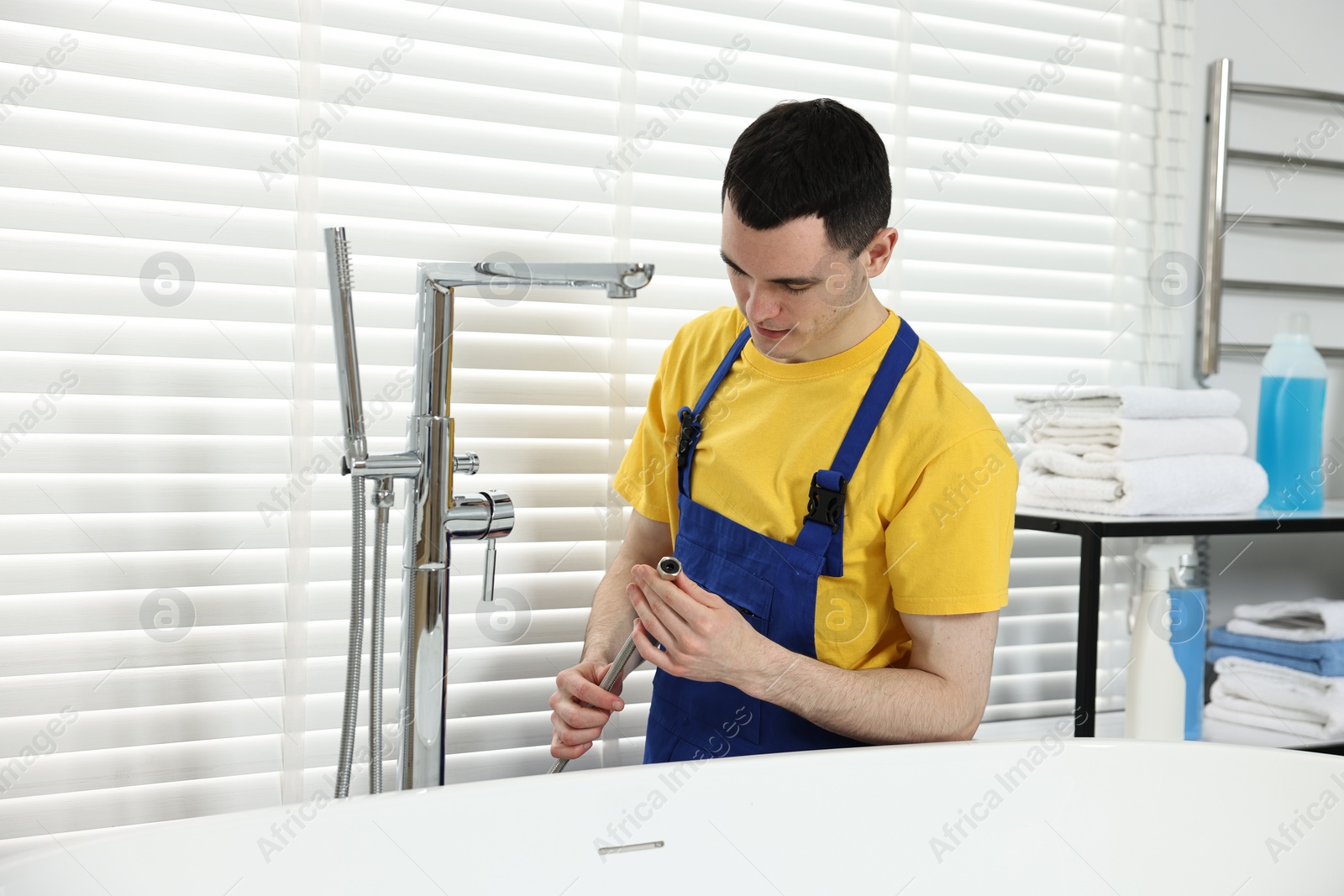 Photo of Young plumber repairing metal faucet in bathroom
