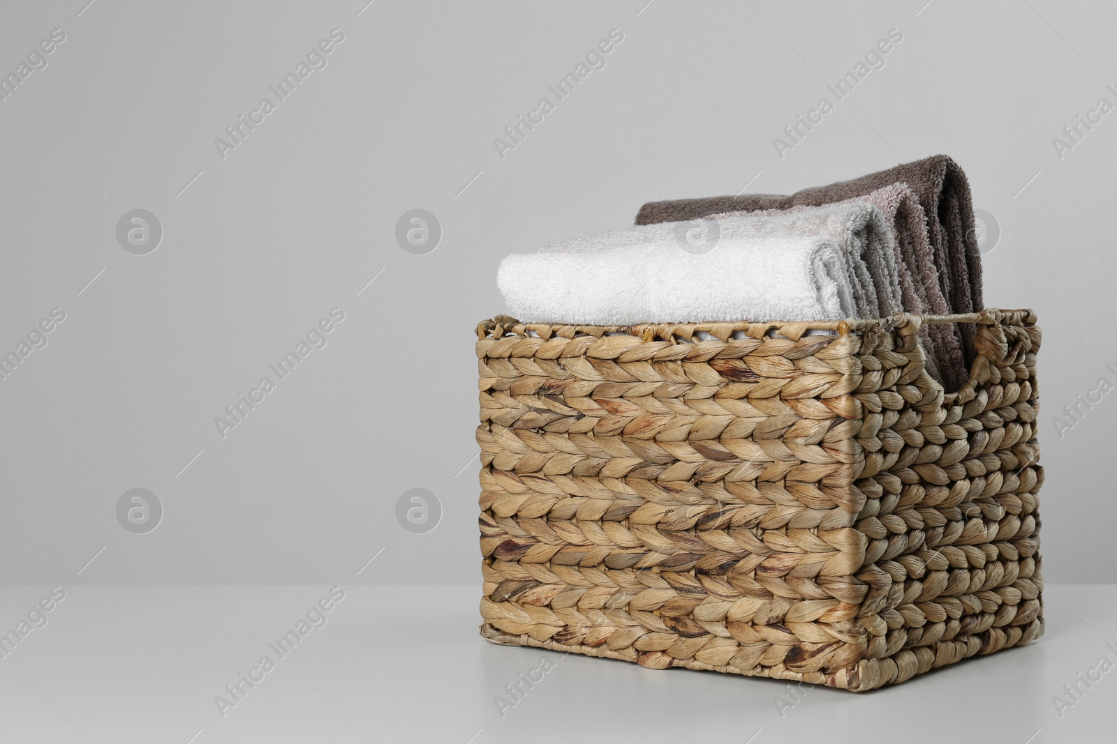Photo of Wicker basket with clean soft towels on light background. Space for text