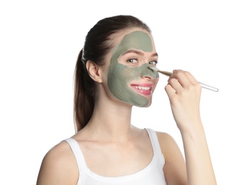 Photo of Young woman applying clay mask on her face against white background. Skin care