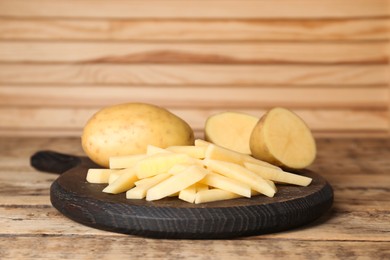 Photo of Whole and cut potatoes on wooden table. Cooking delicious french fries