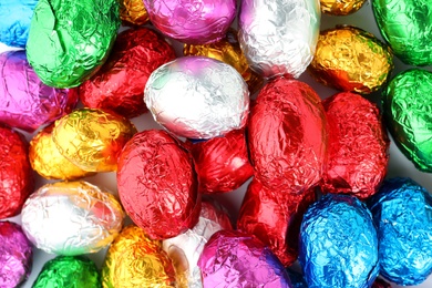 Many chocolate eggs wrapped in bright foil as background, top view