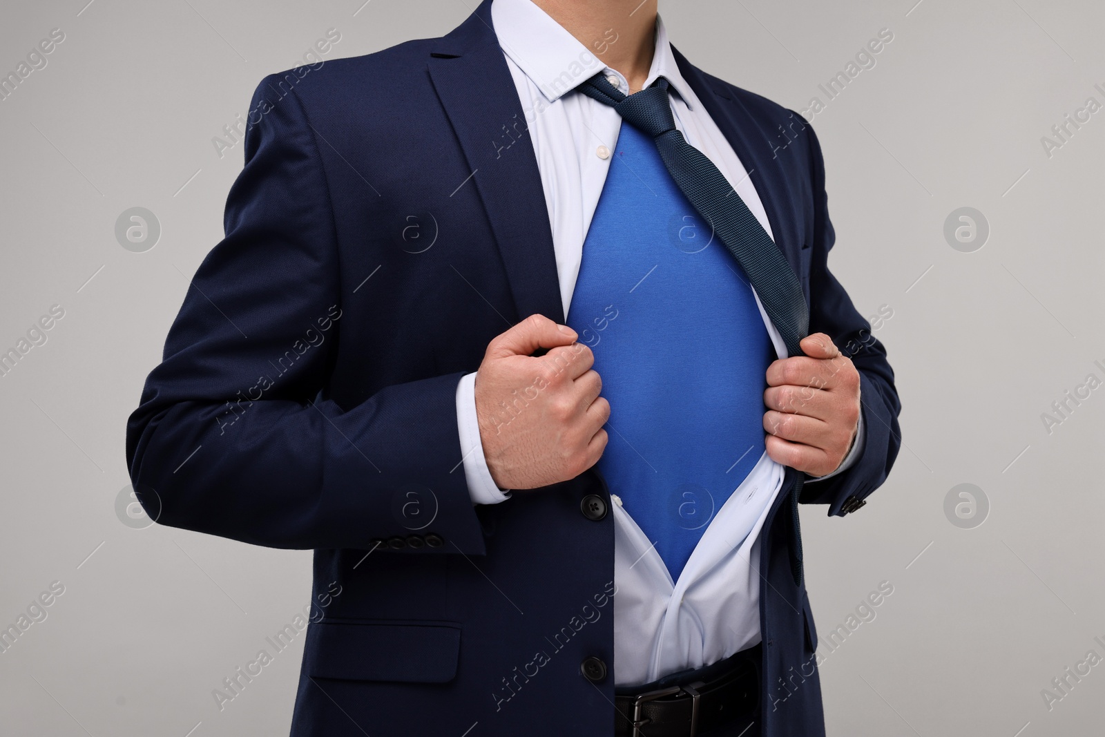 Photo of Businessman wearing superhero costume under suit on beige background, closeup