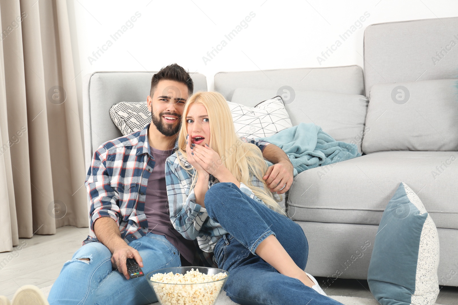 Photo of Young couple with bowl of popcorn watching TV on floor at home