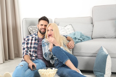 Young couple with bowl of popcorn watching TV on floor at home