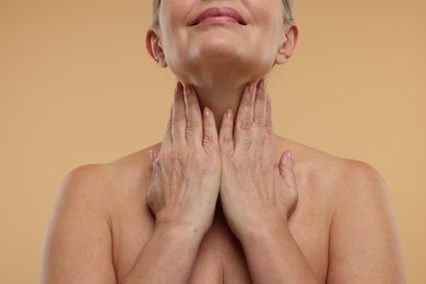 Photo of Mature woman touching her neck on beige background, closeup