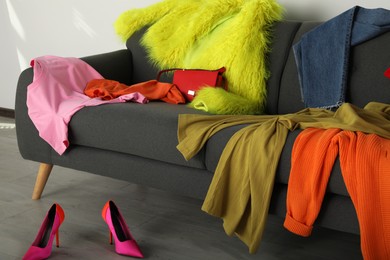 Photo of Messy pile of colorful clothes on sofa and shoes in living room