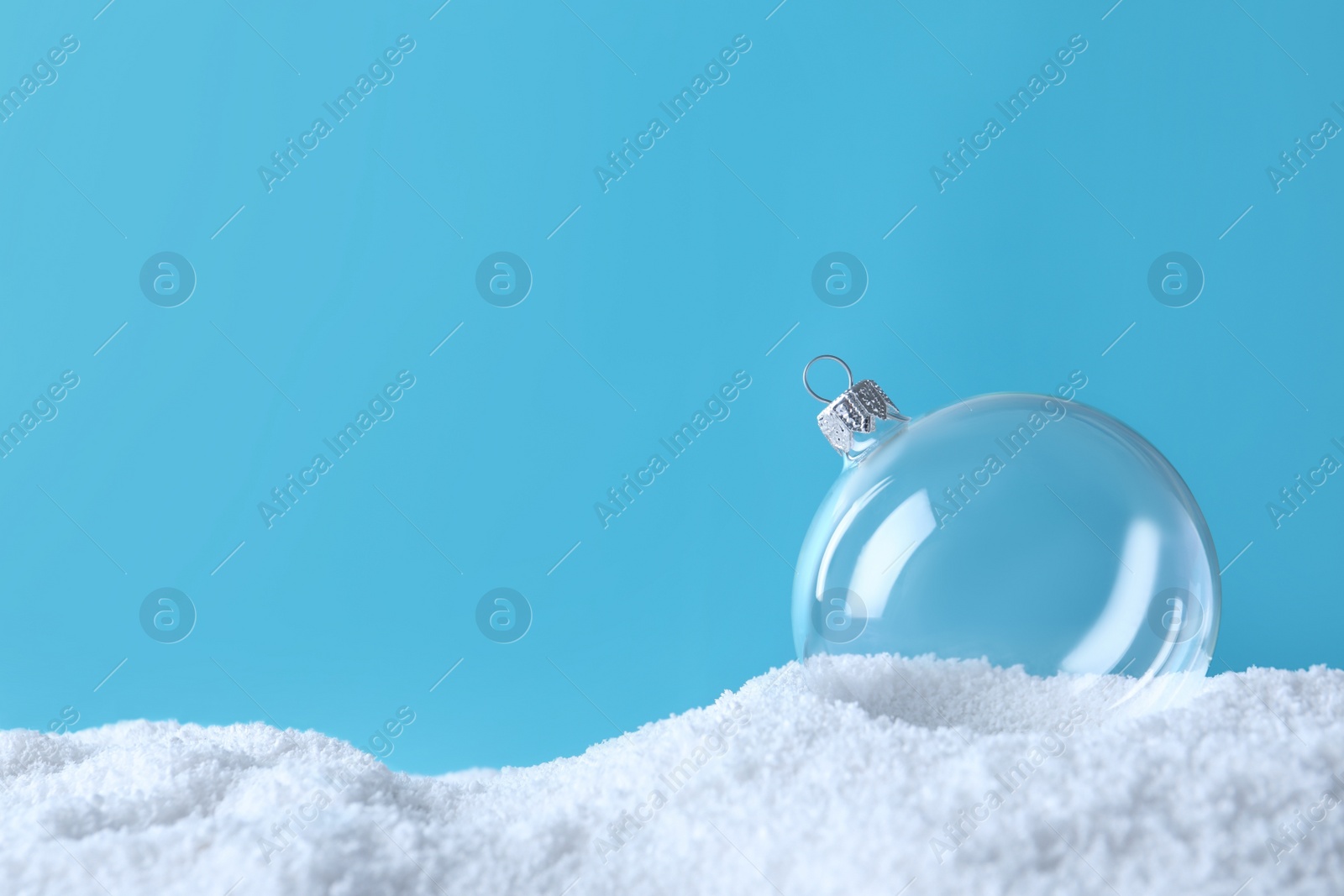 Photo of Transparent Christmas ball on snow against light blue background, space for text