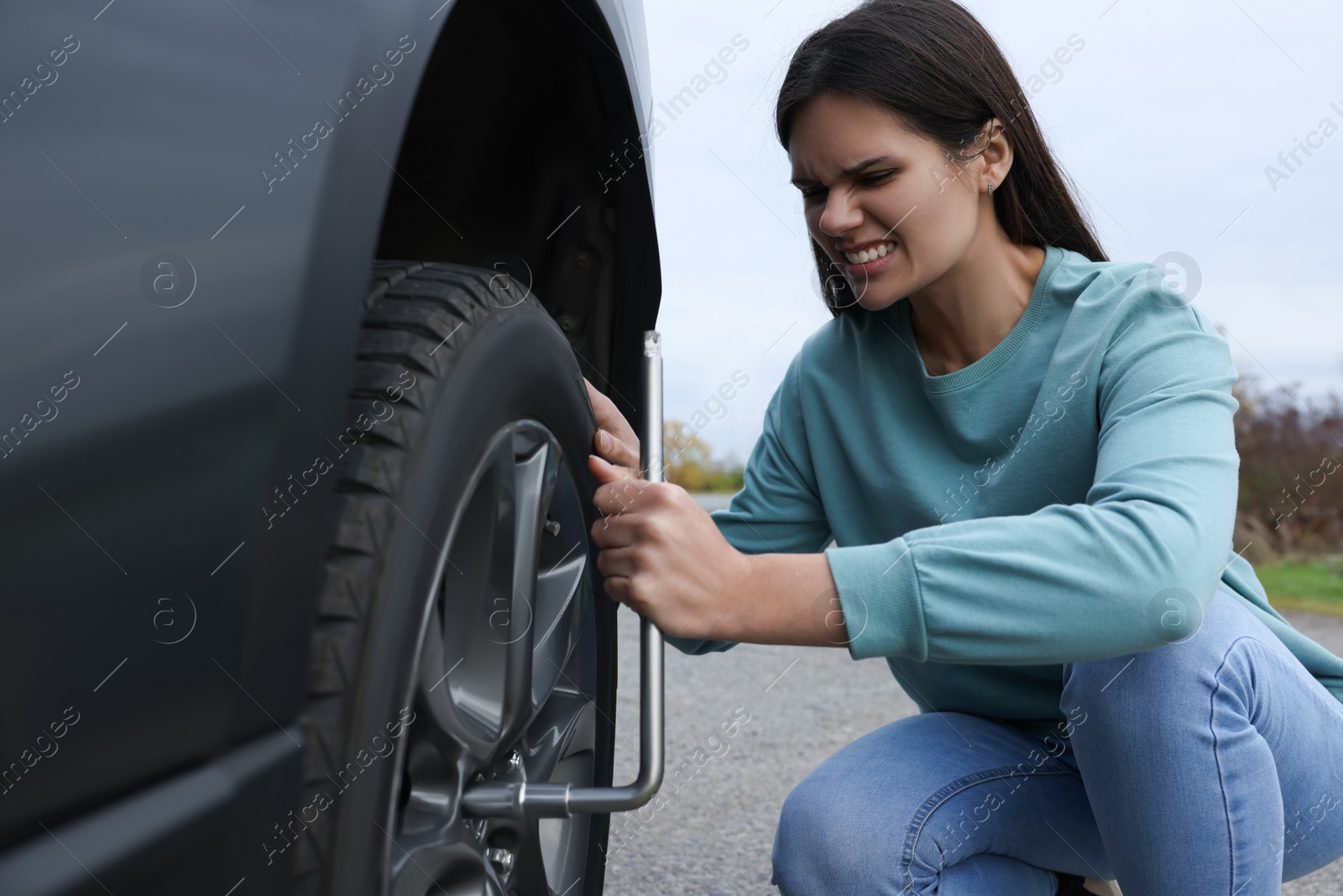 Photo of Young woman changing tire of car outdoors