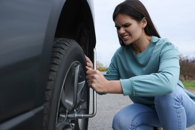 Photo of Young woman changing tire of car outdoors