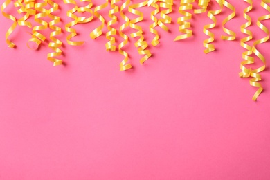 Photo of Yellow serpentine streamers on pink background, flat lay. Space for text