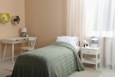 Photo of Stylish room interior with bed, table and air humidifier
