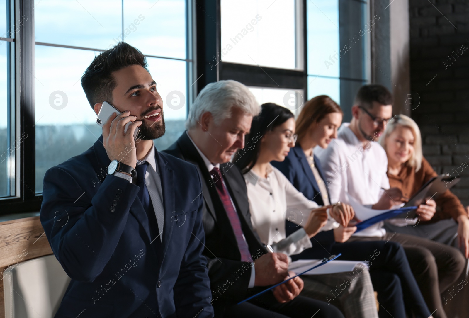 Photo of Young man talking on phone while waiting for job interview in office hall