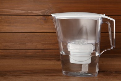 Filter jug with purified water on wooden table. Space for text