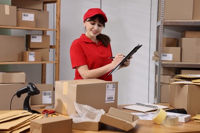 Photo of Parcel packing. Post office worker with clipboard at wooden table indoors