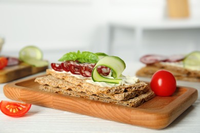 Photo of Fresh rye crispbreads with salami, cream cheese and cucumber on white wooden table, closeup