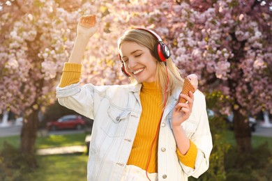 Young woman with ice cream and headphones listening to music outdoors on sunny day