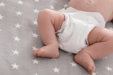 Photo of Cute little baby in diaper lying on bed, closeup
