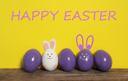 Image of Two eggs with ears as Easter bunnies among others on wooden table against yellow background