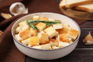 Photo of Delicious crispy croutons with rosemary in bowl on wooden table, closeup