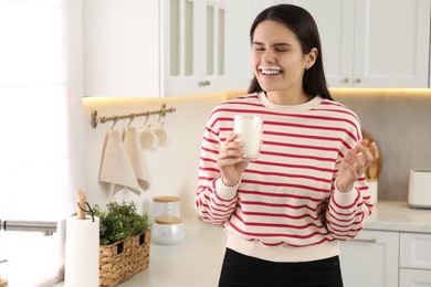 Happy woman with milk mustache holding glass of tasty dairy drink in kitchen. Space for text